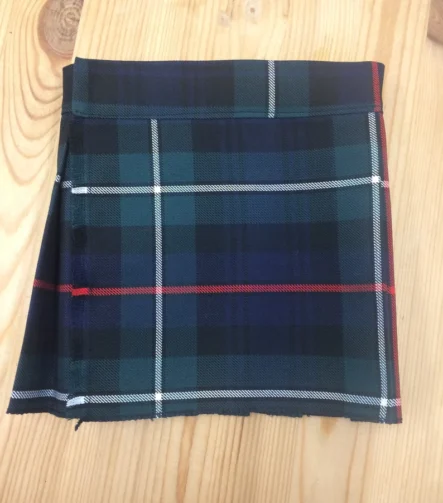 Children's MacKenzie tartan kilt in blue, green, red and white plaid folded on wooden background